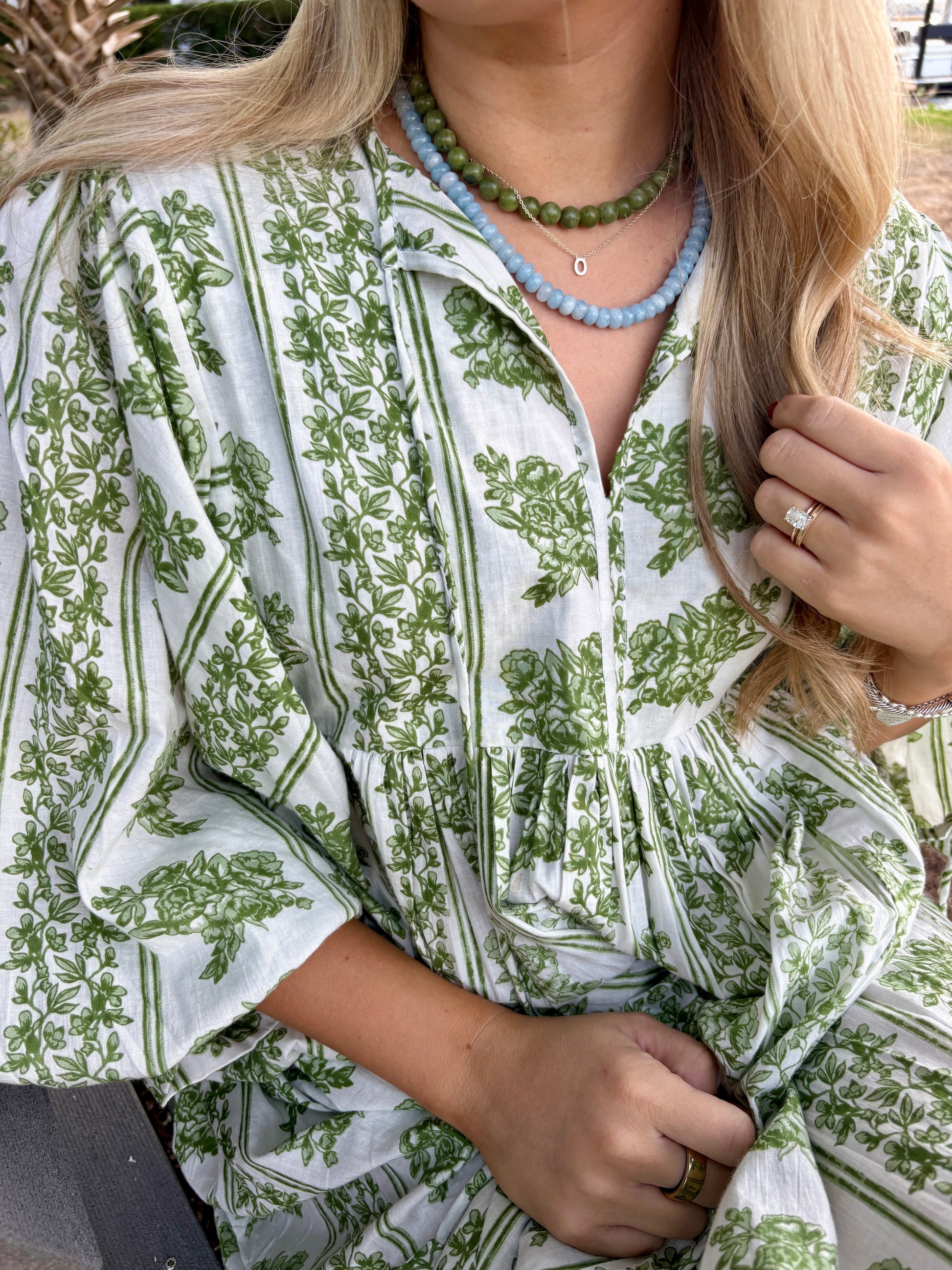 Person wearing a green and white patterned dress with a necklace.